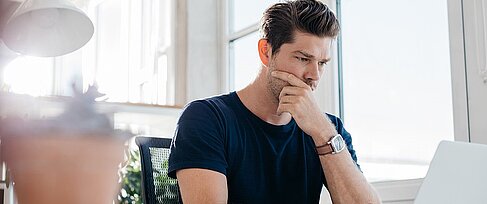 Mann liest konzentriert am Laptop.